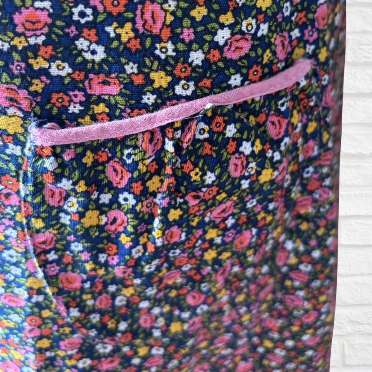 Close-up of a floral  dress fabric panel with a dense multicolour print on a dark navy background and a pink trim detail.
