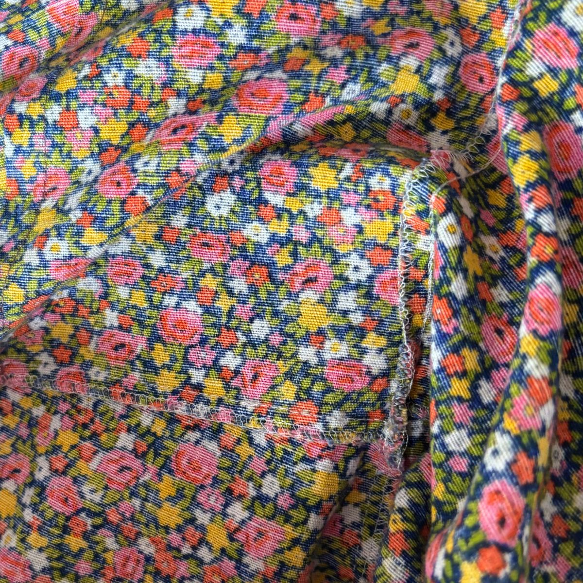 Close-up of a multicolor floral fabric with pink, yellow, orange, and white flowers on a dark navy background, showing the woven texture and a folded seam.
