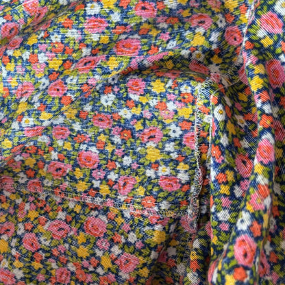 Close-up of a multicolor floral fabric with pink, yellow, orange, and white flowers on a dark navy background, showing the woven texture and a folded seam.