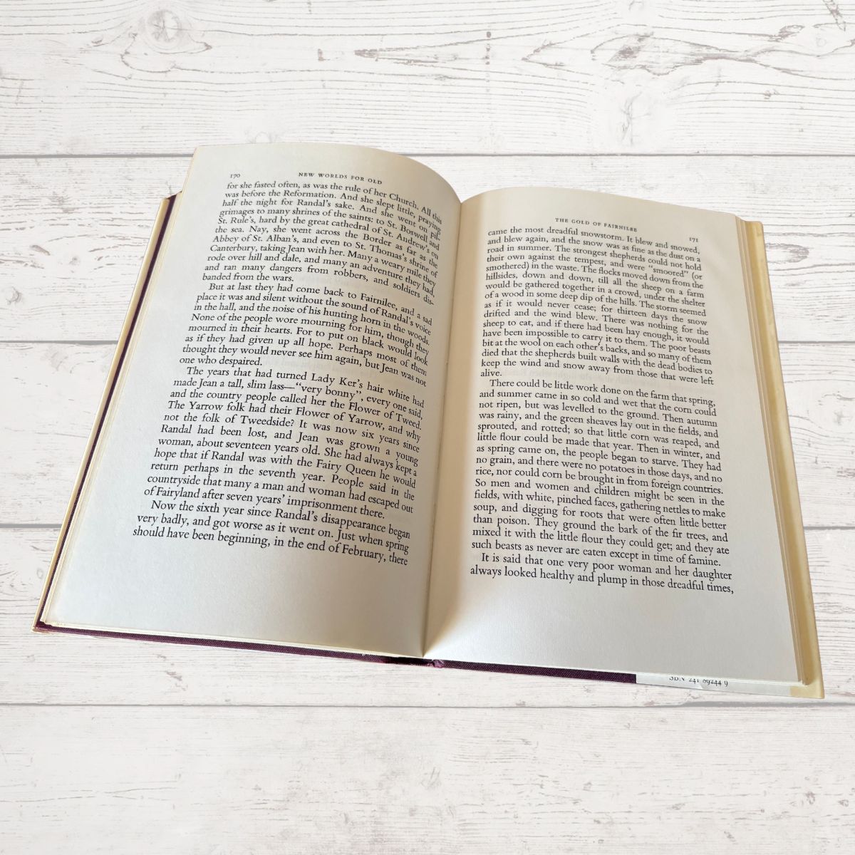 An open hardcover book showing two open pages with printed text, photographed from above on a light whitewashed wood surface.