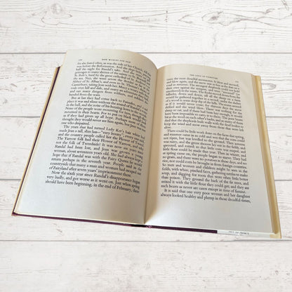 An open hardcover book showing two open pages with printed text, photographed from above on a light whitewashed wood surface.