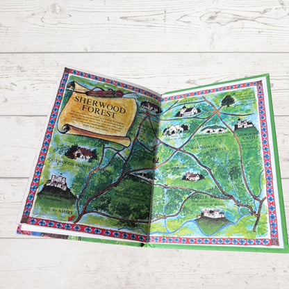 An open illustrated map book titled 'Sherwood Forest' laid flat on a light whitewashed wood surface. The pages show a colorful fantasy-style forest map with trees, paths, houses, and castle illustrations.