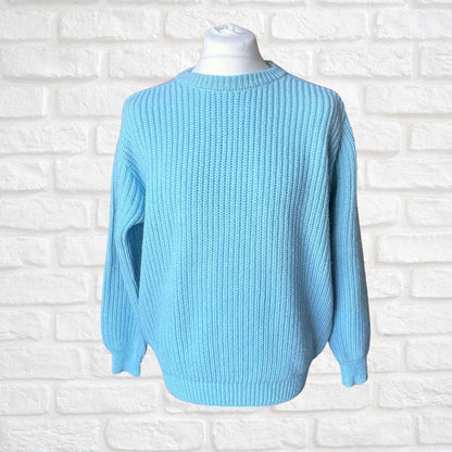 A light blue ribbed knit sweater displayed on a white mannequin torso against a white painted brick wall background.