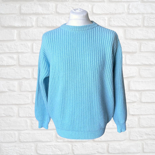 A light blue ribbed knit sweater displayed on a white mannequin torso against a white painted brick wall background.