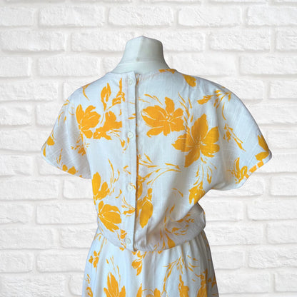White dress with yellow floral pattern on a white brick wall background