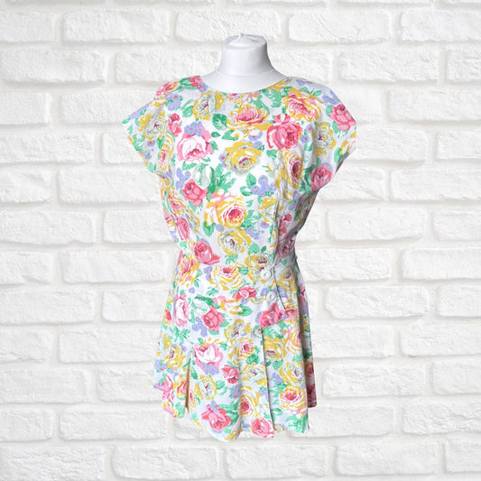A short-sleeve peplum dress with a colorful floral print, displayed on a white mannequin torso against a white brick wall background.