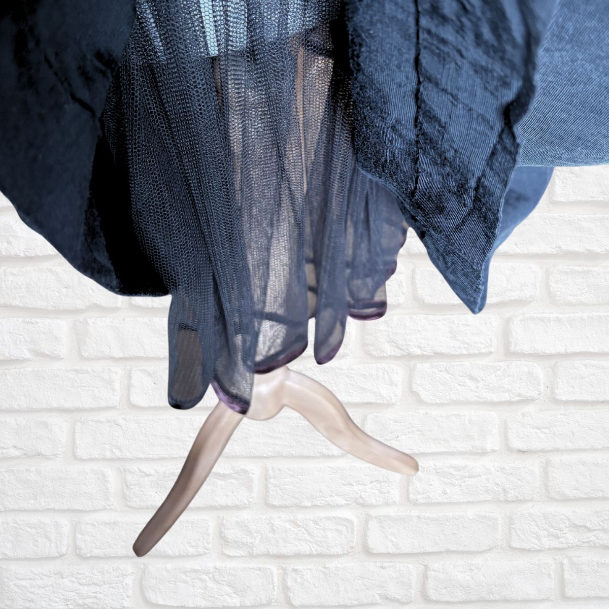 A close-up of a black sheer mesh fabric draped over a light beige hanger, set against a white brick wall background.
