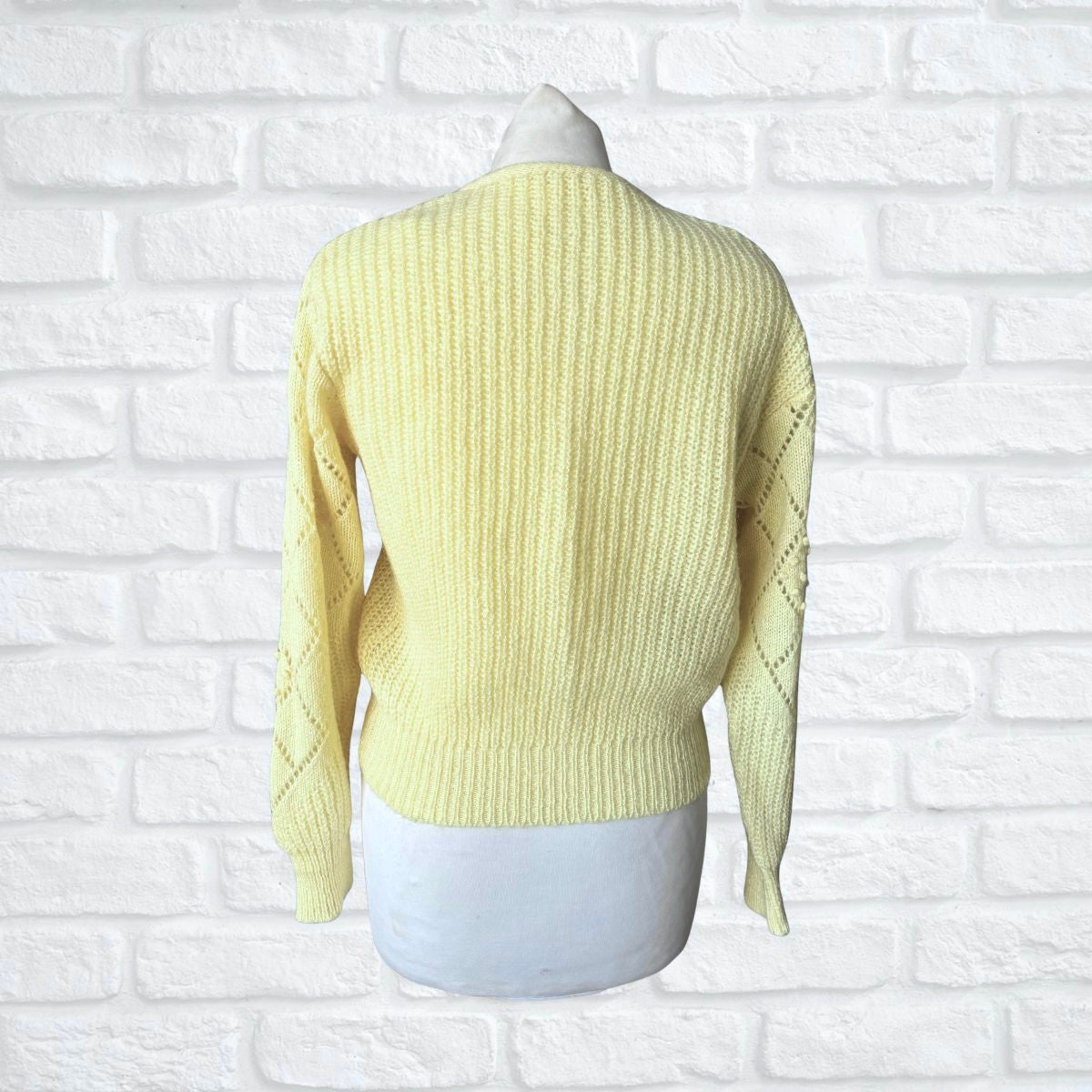 Light yellow sweater on a mannequin against a white brick wall background