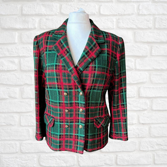 A women's double-breasted blazer in a green and red tartan plaid pattern, displayed on a white mannequin torso against a white brick wall background.
