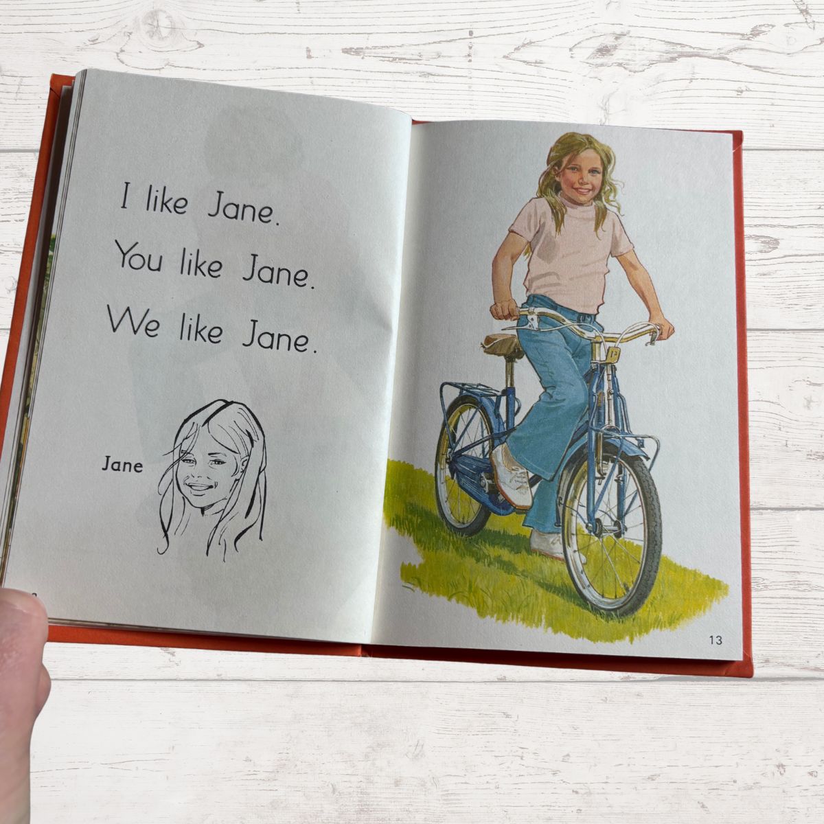 Open book with illustrations of a girl on a bike and text about 'Jane'.