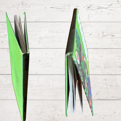 A bright green book standing open in two views against a light wood plank background, showing the colorful illustrated cover 
