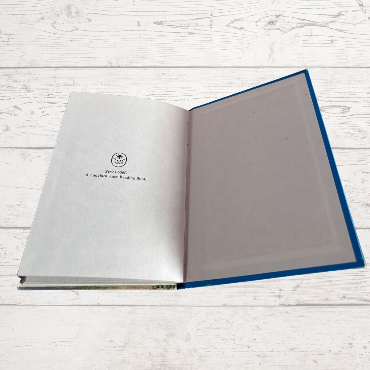 An open children's book titled 'A Ladybird Key-Reading Book' featuring a blue hardcover and blank interior pages, displayed on a white wood plank background.