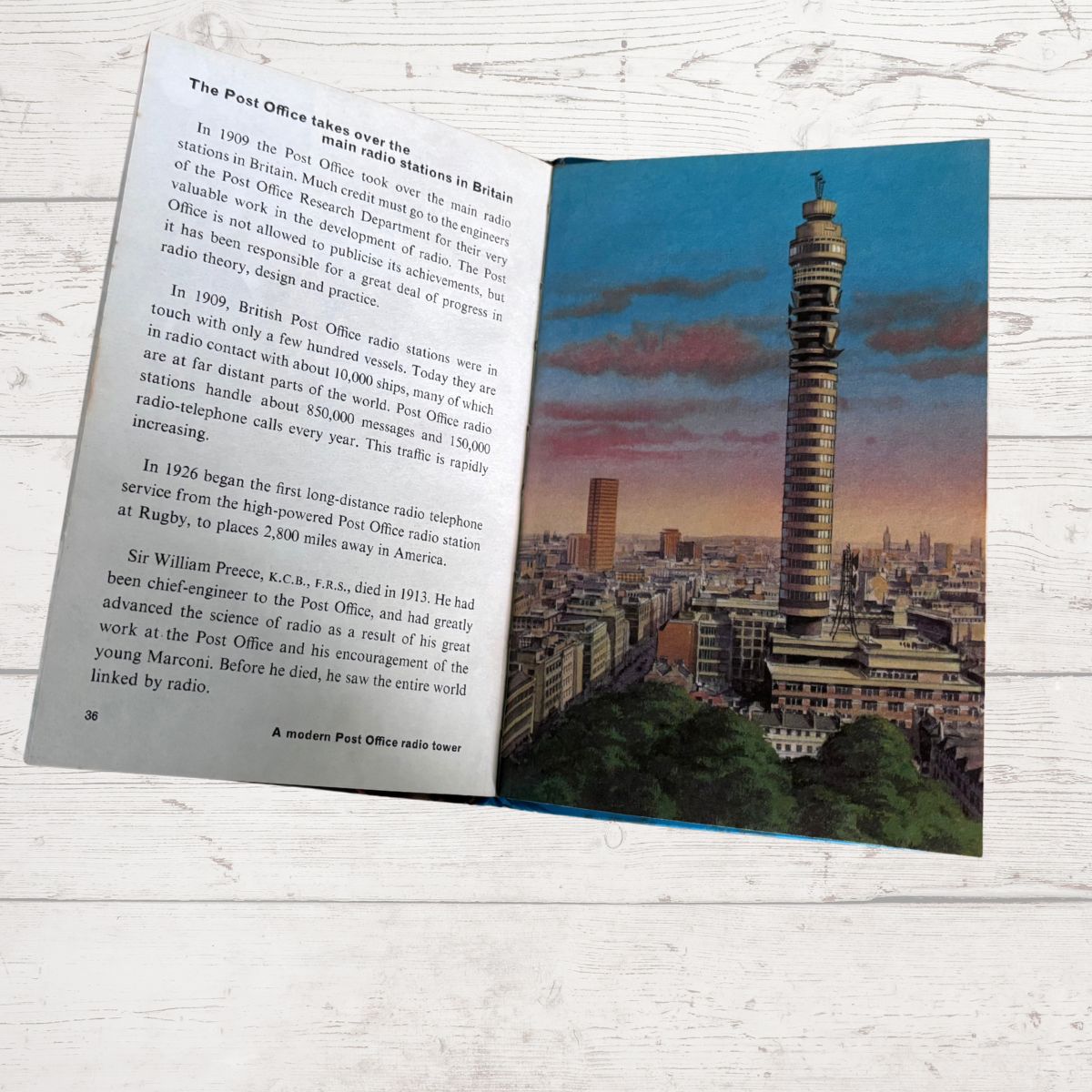 An open book oon a white wood surface, showing printed text on the left page and a color photograph of a tall tower and city skyline on the right