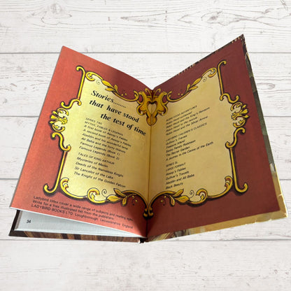 An open book spread showing decorative gold borders and printed text on red and gold pages, photographed on a light wood surface.