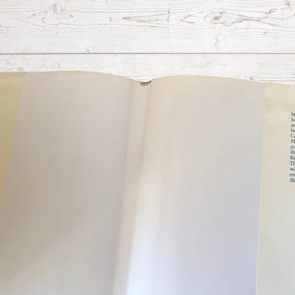 An open book with blank cream-colored pages, photographed from above on a white wooden surface.