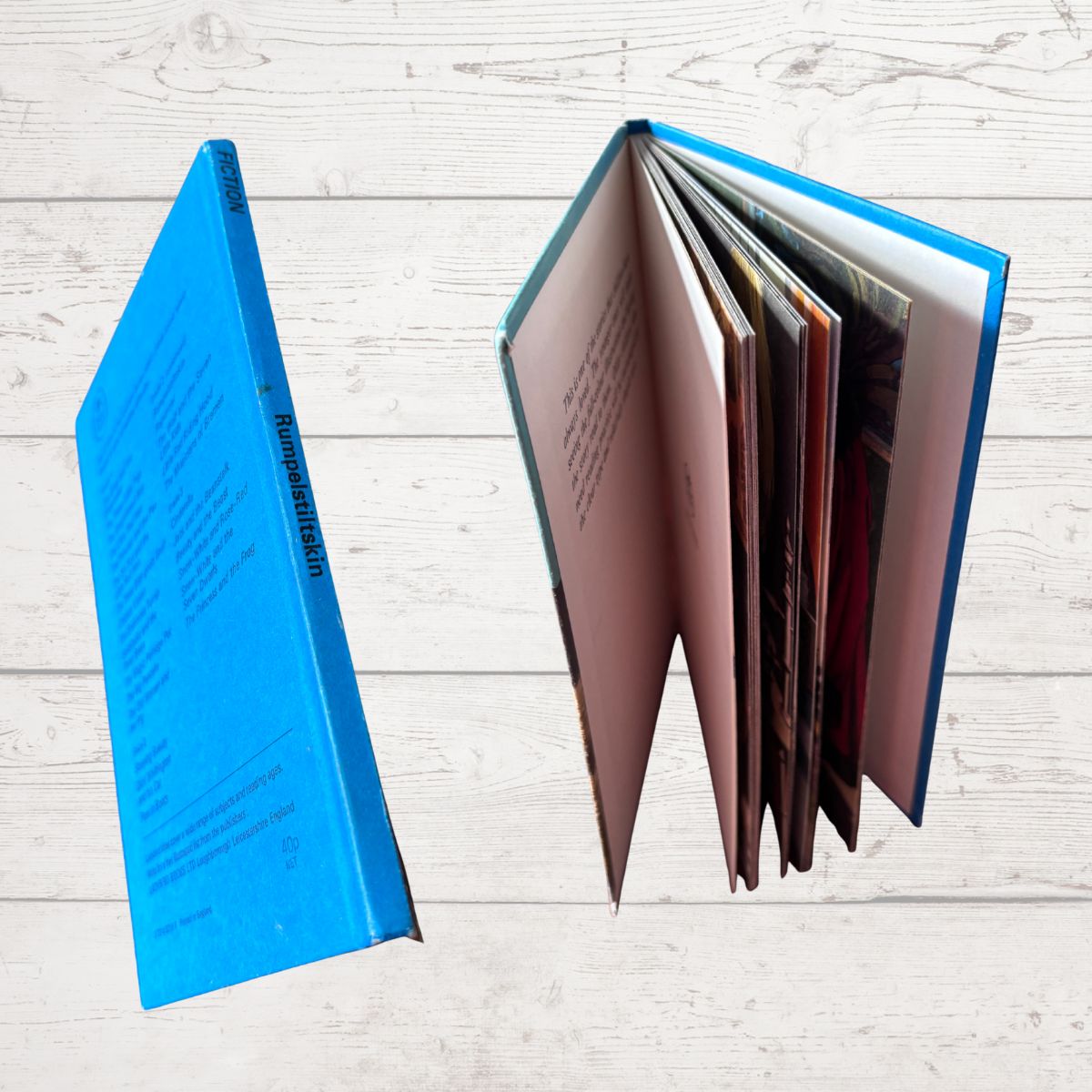 A blue hardcover book shown open on a light wood plank background, with the back cover visible on the left and several interior pages fanned out on the right.