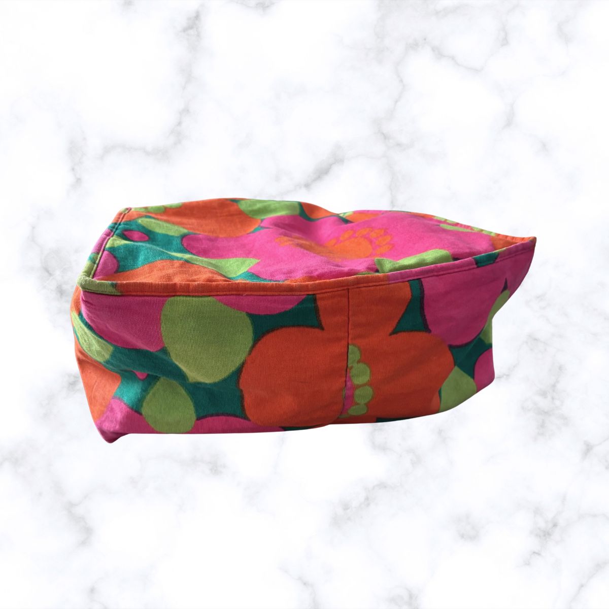 A bag with a bold retro floral pattern in pink, orange, green, and dark teal, set against a white marble background