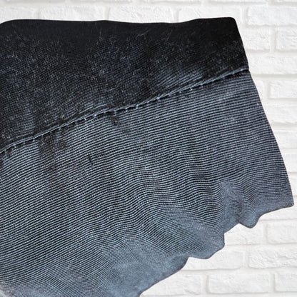A close-up of a dark black textured fabric with a visible stitched seam, laid against a white brick wall background.