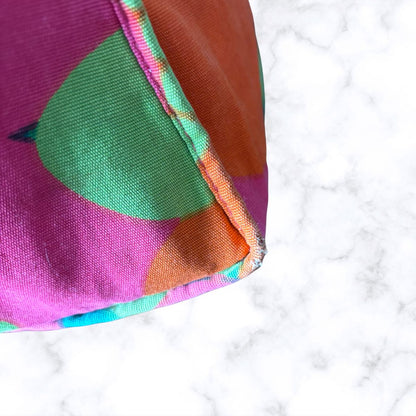 A close-up of a bag corner, featuring a bold geometric pattern in magenta, green, orange, and turquoise, resting on a white marble 