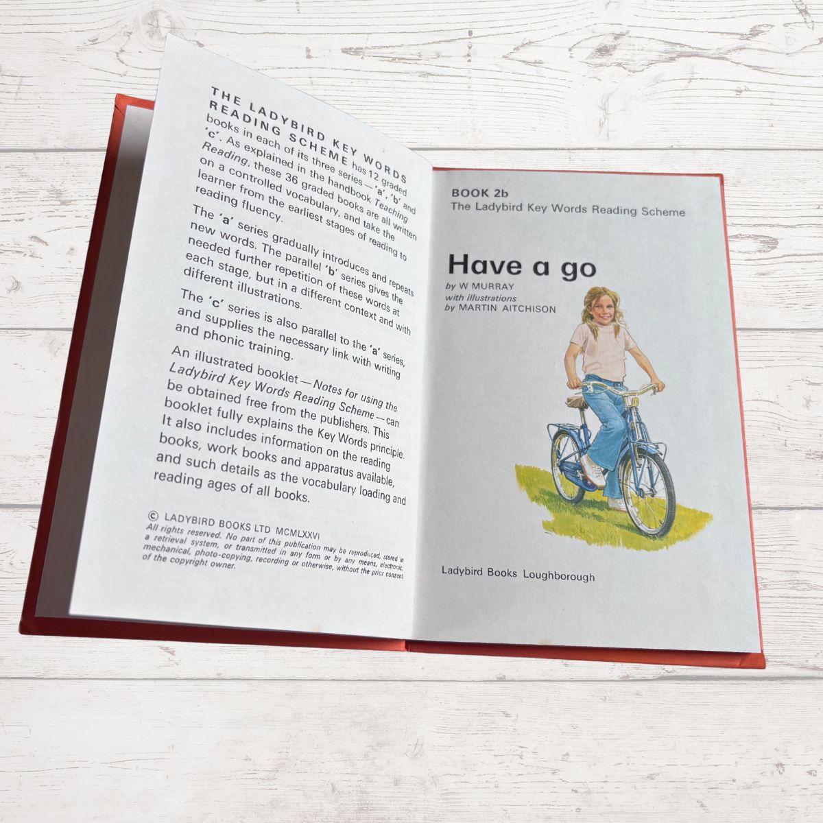 Open book with text and illustration of a person on a bicycle, on a light wooden surface.