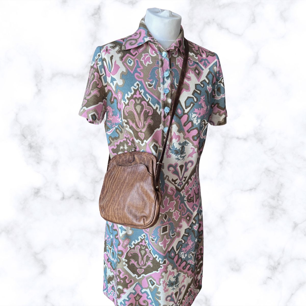 Mannequin wearing a patterned dress with a brown handbag on a white background