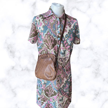 Mannequin wearing a patterned dress with a brown handbag on a white background