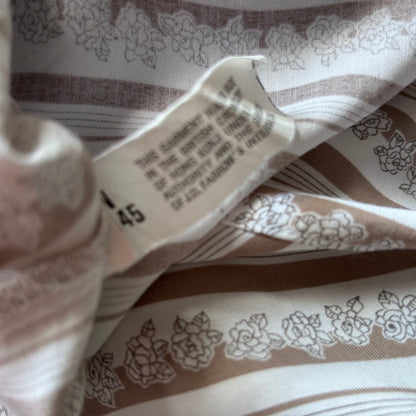 Close-up of a garment's inner label sewn onto patterned fabric. The fabric is cream and taupe with a floral line-art print.