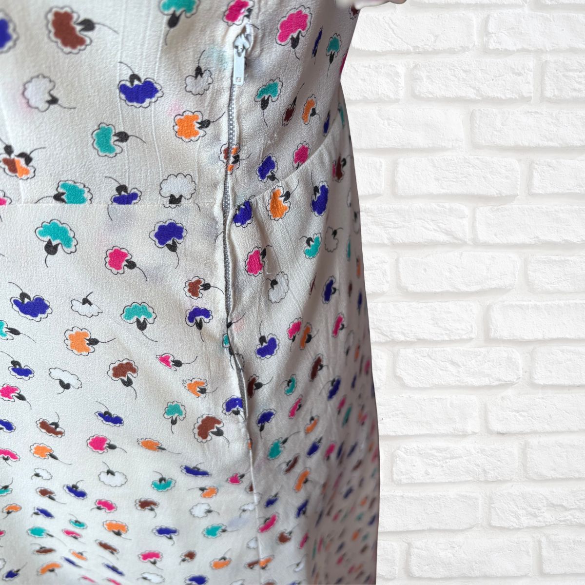 Close-up of a dress with colorful floral pattern against a white brick wall.