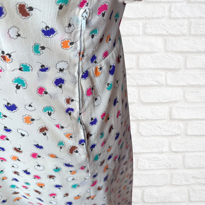 Close-up of a dress with colorful floral pattern against a white brick wall.