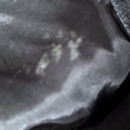 A close-up of a dark gray or black textured fabric surface with a subtle woven or mesh-like pattern.