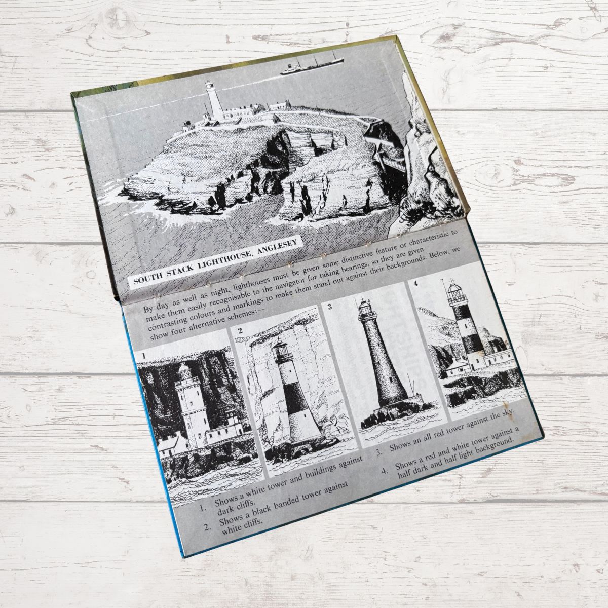 A rectangular printed book inside cover  showing black-and-white historical lighthouse illustrations and descriptive text, photographed on a light whitewashed wood 