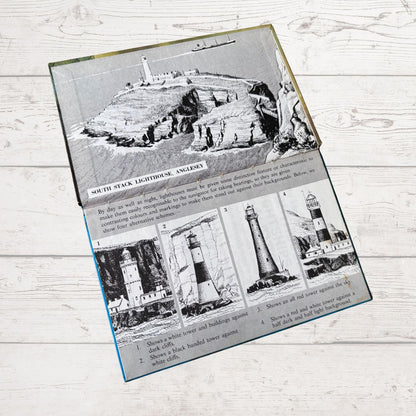 A rectangular printed book inside cover  showing black-and-white historical lighthouse illustrations and descriptive text, photographed on a light whitewashed wood 