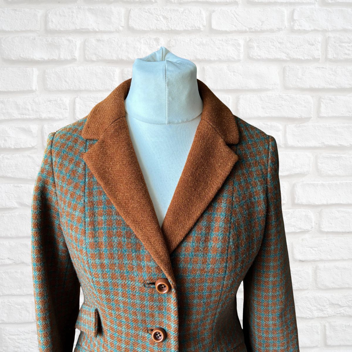 Mannequin wearing a brown and blue checkered coat against a white brick wall.
