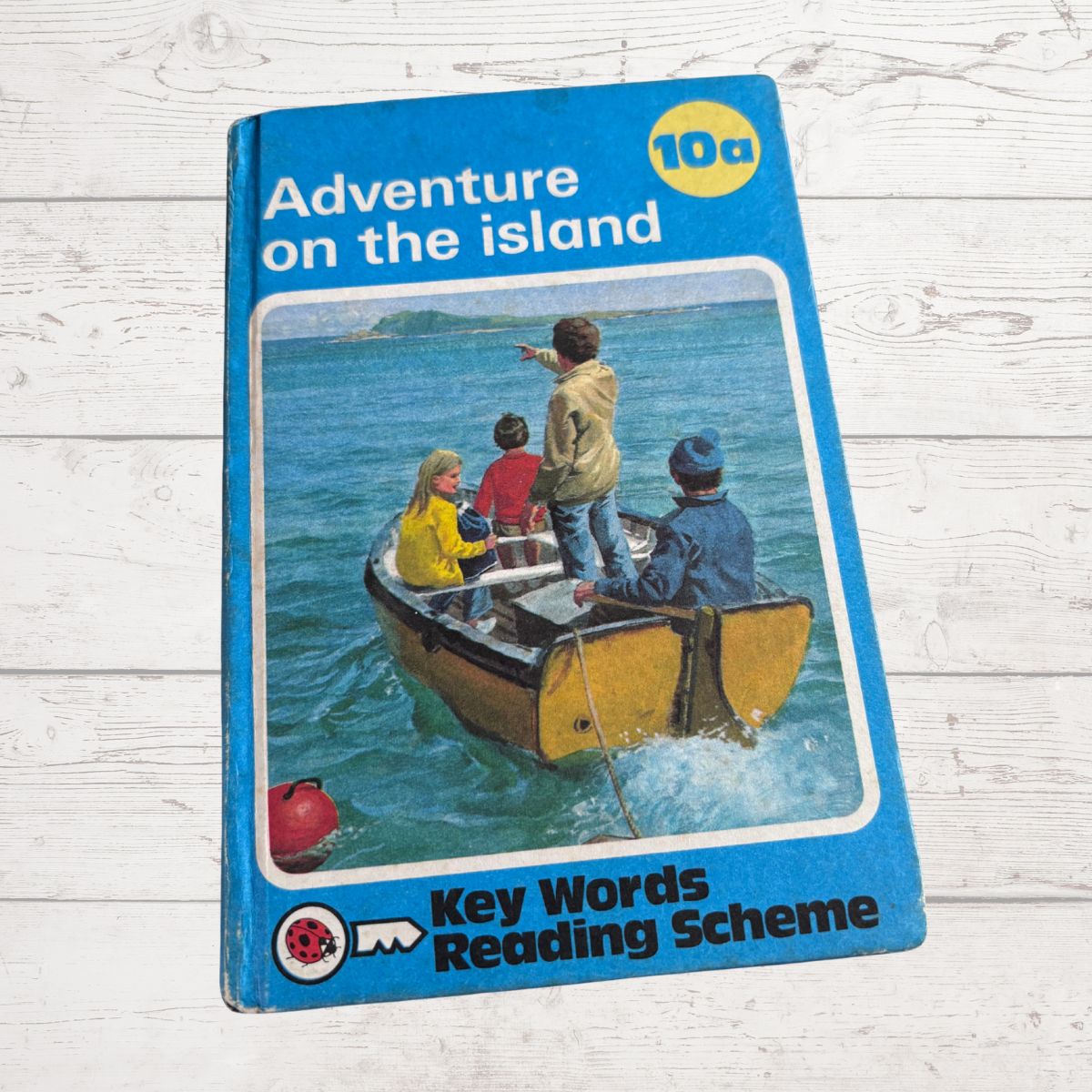 Book cover of 'Adventure on the Island' from Key Words Reading Scheme on a wooden surface