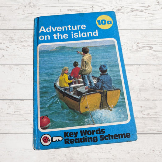 Book cover of 'Adventure on the Island' from Key Words Reading Scheme on a wooden surface