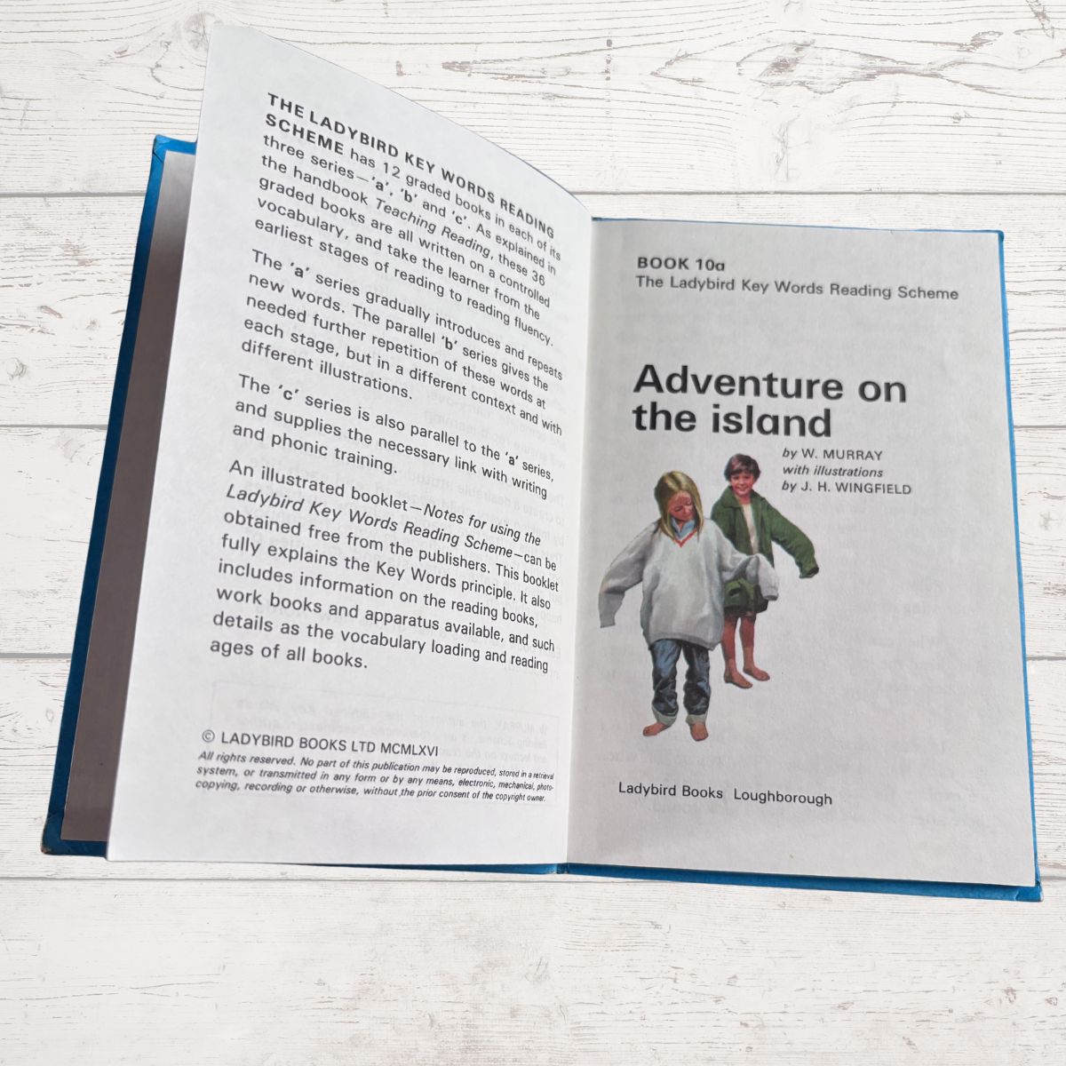 Open book showing a Ladybird Books reading scheme book titled 'Adventure on the Island' on a wooden surface.