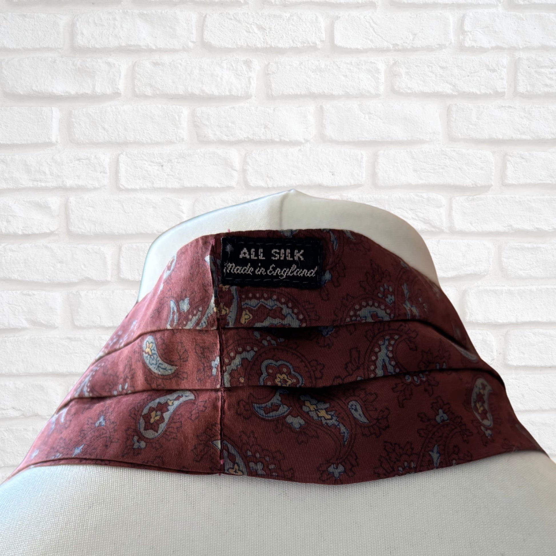 The back of vintage silk cravat featuring a paisley print in red, grey, yellow, and blue with an all silk and made in England label 