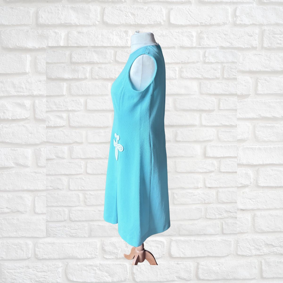 Turquoise dress with a white 3 D design on a white brick wall background