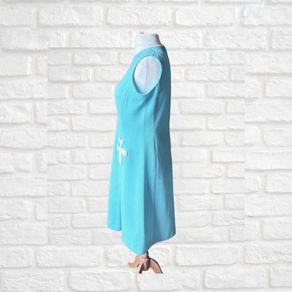 Turquoise dress with a white 3 D design on a white brick wall background