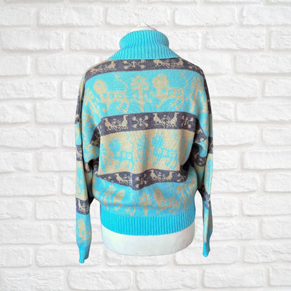 A turquoise blue and beige knit sweater with a dark gray patterned band, displayed on a white mannequin torso against a white brick wall background.