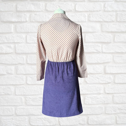 Mannequin wearing a two-tone dress with a geometric print top and solid purple skirt against a white brick wall.