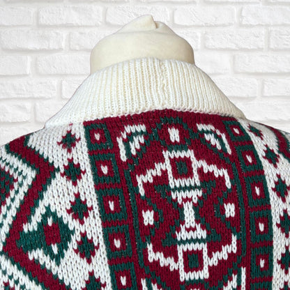 A close-up of a knit sweater on a cream-colored mannequin torso, showing a festive Christmas pattern in burgundy red, white, and dark green. The background is a white brick wall.