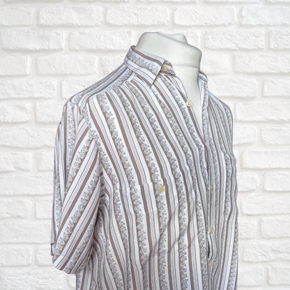 A short-sleeve button-up shirt with vertical stripes of brown, beige, and white, featuring a  floral pattern , displayed on a white mannequin torso against a white brick wall background.