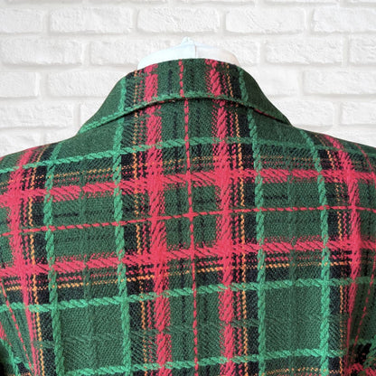 A close-up of a green plaid jacket against a white brick wall background.