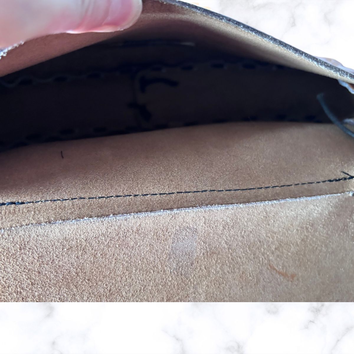 Close-up of a bag interior, showing a stitched edge and dark lining, with a finger holding the opening at the top.