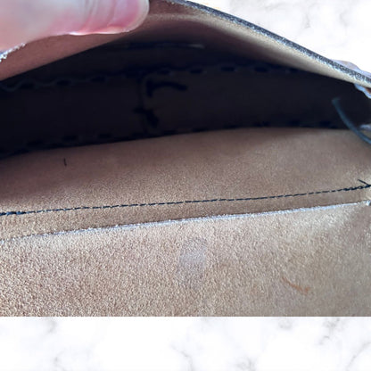 Close-up of a bag interior, showing a stitched edge and dark lining, with a finger holding the opening at the top.