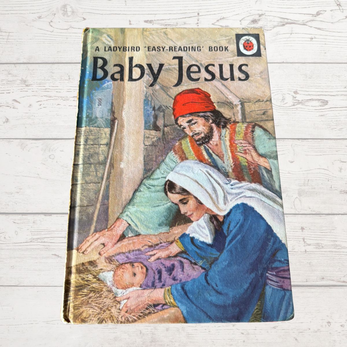 Book titled 'Baby Jesus' with illustrations of a woman and man holding a baby on a wooden surface.