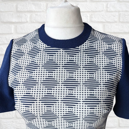 Mannequin wearing a blue and white patterned top against a white brick wall.