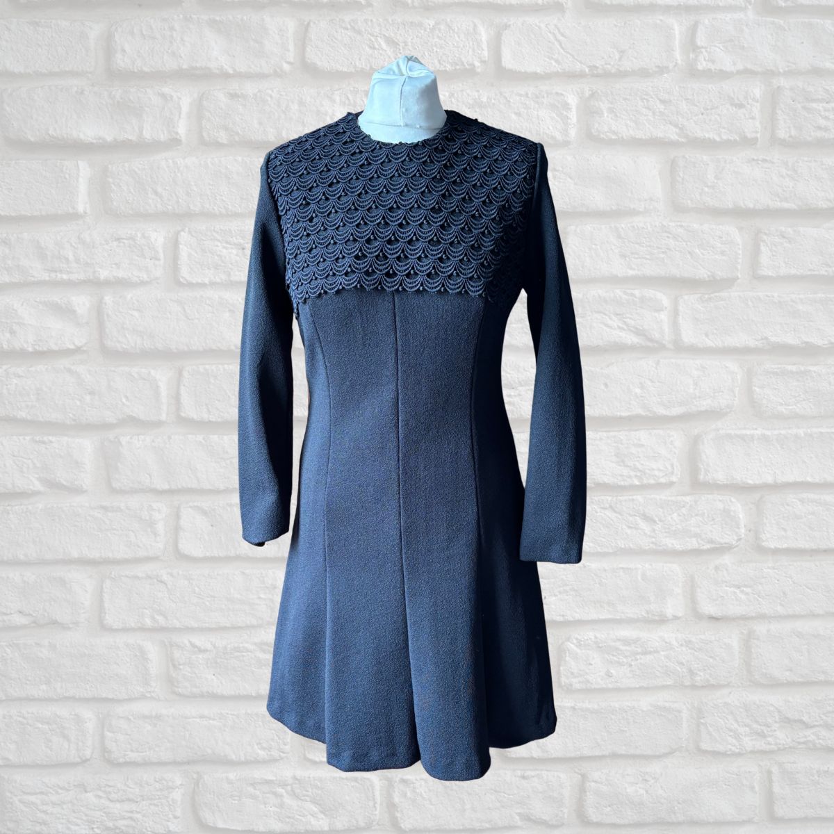 Black  dress with a textured neckline on a white brick wall background