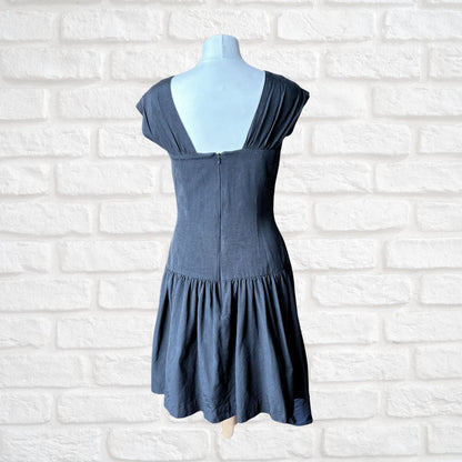 A black dress displayed on a mannequin’ against a white brick wall background